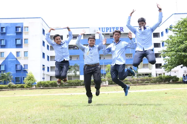 Four students jumping in the air on the lawn in front of the college building.
