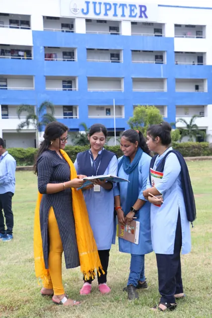 A teacher and students reviewing notes outside the college building.