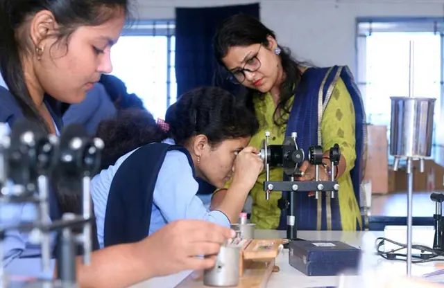 A student taking a reading on physics apparatus while a teacher watches.