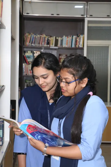 Two students reading a book together in front of the library shelves.